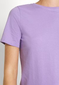 Fioletowa bawełniana koszulka z krótkimi rękawami, okrągłym dekoltem, gładką fakturą i prostym designem. Brak widocznych wzorów lub grafik.