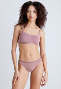 Light pink wireless bra and matching low-rise brief displayed on a person. Material appears soft with thin straps and elastic trim details.