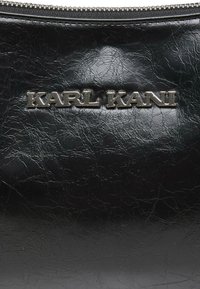 Czarna skórzana torba z teksturowanym wykończeniem, srebrnym logo "KARL KANI" i zamknięciem na zamek błyskawiczny. Design jest elegancki i funkcjonalny.