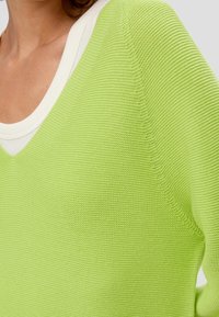 Limegrüner, leichter Strickpullover mit V-Ausschnitt und weißem Innenfutter, der ein strukturiertes Muster und eine lockere Passform aufweist.