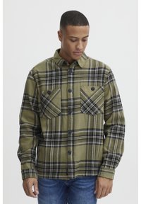 Grüne Karobluse aus Flanell, mit zwei Brusttaschen, schwarzen Knöpfen und kontrastierenden schwarz-weißen Streifen im Muster.