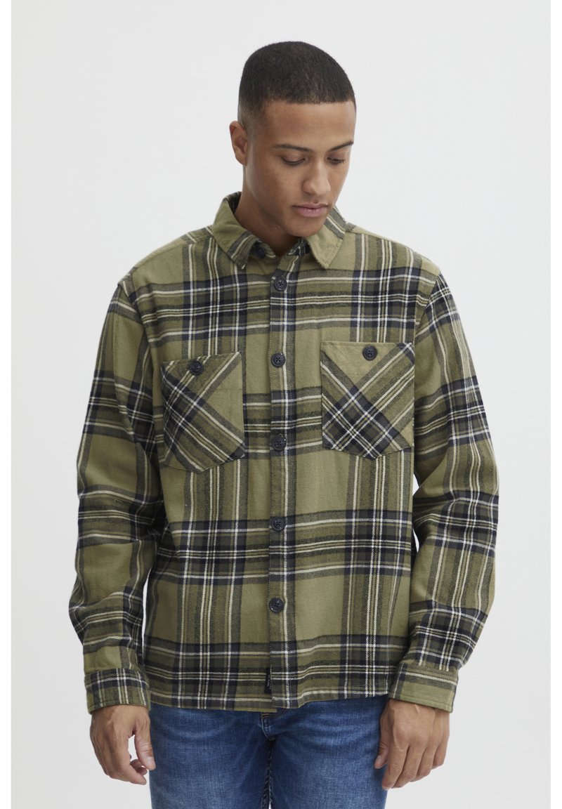 Grüne Karobluse aus Flanell, mit zwei Brusttaschen, schwarzen Knöpfen und kontrastierenden schwarz-weißen Streifen im Muster.