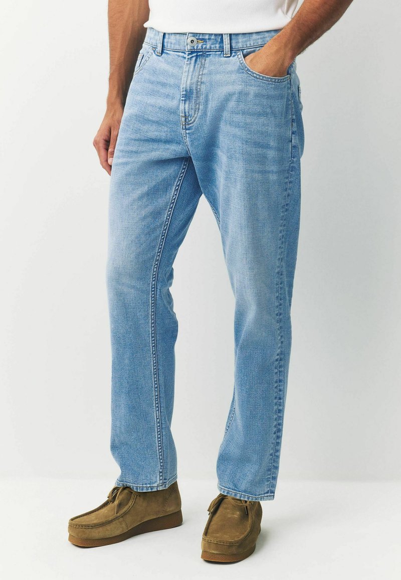 Világoskék farmernadrág, egyenes szabással, öt zsebes dizájnnal, finom kopással és látható varrásokkal. Barna velúr slip-on cipővel párosítva.