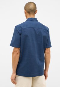Koszulka z krótkim rękawem w ciemnoniebieskim kolorze, wykonana z teksturowanej tkaniny, z kołnierzykiem typu spread i detalem na plecach. Prosty, czysty design bez wzorów.
