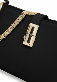 Borsa sintetica nera con tracolla in catena dorata, caratterizzata da una chiusura rettangolare dorata e logo del marchio impresso sul davanti.