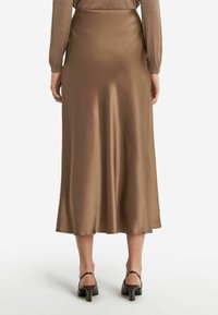 Jupe longue en satin marron avec une texture lisse, design fluide et coupe mi-longue, associée à des talons noirs épurés.