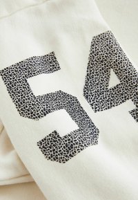 Svart och mörkbeige prickig siffra "54" tryckt på ljusbeige texturerad tyg.