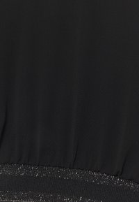 Černá tkanina s hladkým povrchem má naškrobený pas s lesklým, třpytivým detailem. Materiál je lehký a jemně se splétá.