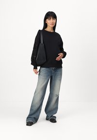 Black oversized sweatshirt with eyelet detail on sleeves, paired with light blue wide-leg jeans; model carries a black tote bag.
