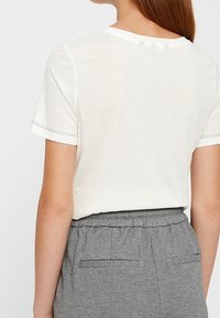 Vit kortärmad t-shirt med rund hals och subtila sömdetaljer, kompletterad av grå byxor med elastisk midja och bakfickor.