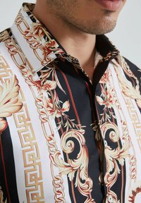 Chemise à manches courtes noir et blanc avec des motifs floraux et de chaînes. Dispose d'un col net et de détails en boutons, fabriquée à partir d'un tissu léger.