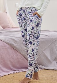 Floral-patterned pants in light pastel colors with purple flowers, made of soft fabric. Includes side pockets and a relaxed fit design.