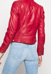 Giubbotto di pelle rossa con accenti trapuntati sulle spalle, design aderente e polsini con cerniera. Abbinato a jeans attillati blu chiaro.