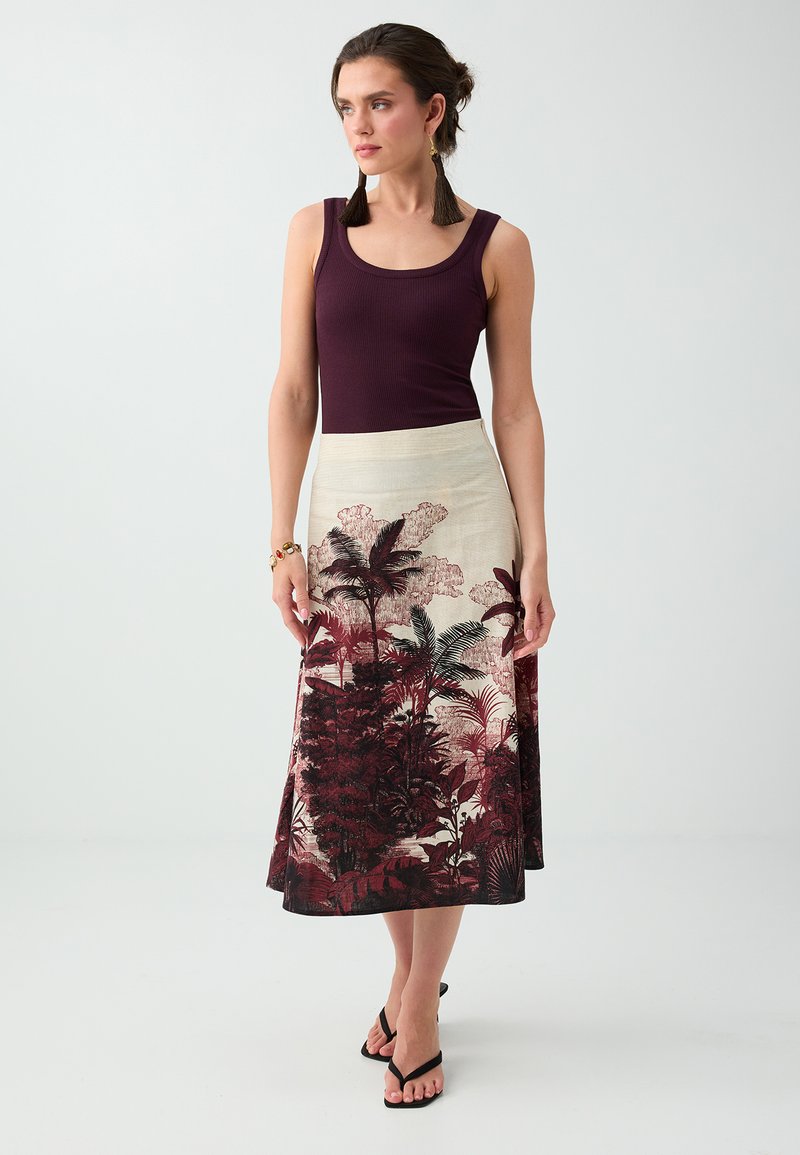 Femme portant un haut violet sans manches assorti à une jupe beige mi-longue avec des imprimés de plantes tropicales rouge foncé et noir.