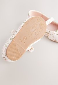 Ballerines blanches à motif floral, intérieur rose pâle, et semelle en caoutchouc texturée. Dotées d'une bride pour un ajustement sécurisé.