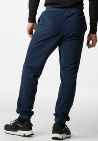 Marineblauwe joggers van zachte stof met een elastische tailleband, zijzakken en taps toelopende boorden. Gecombineerd met zwarte sportschoenen met witte zolen.