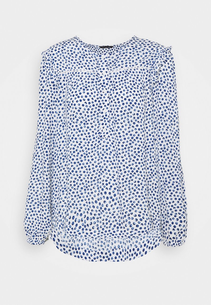Blouse blanche à manches longues avec pois bleus, boutons sur le devant et légers volants aux épaules et aux poignets.