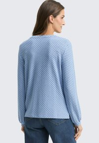 Langärmliges, hellblaues Hemd mit geometrischem Muster, weicher Textur, lockerer Passform und rundem Ausschnitt, kombiniert mit dunkelblauen Jeans.