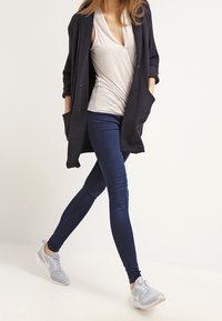 Námořnický cardigan s kapsami přes světle šedý V-krk top, doplněný o tmavě modré skinny džíny a šedé texturované tenisky.