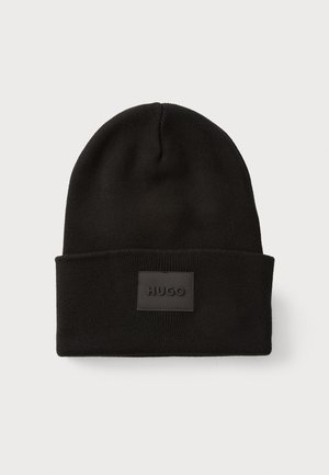 Zwarte gebreide beanie met een omgeslagen rand; heeft een rechthoekig zwart leren label met de opdruk "HUGO" aan de voorkant. Zachte textuur.
