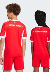 Røde FC Bayern München sportsdrakter med hvite detaljer, kortermet, og matchende shorts, med "FC BAYERN MÜNCHEN" på ryggen.