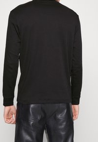 Schwarzes Langarmshirt mit rundem Ausschnitt und gerippten Bündchen, kombiniert mit glänzenden schwarzen Lederhosen mit Gesäßtaschen und Nähdetails.