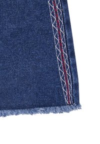 Tessuto denim di colore blu scuro, con bordi sfrangiati. Cuciture decorative rosse e bianche lungo la cucitura laterale aggiungono dettagli.