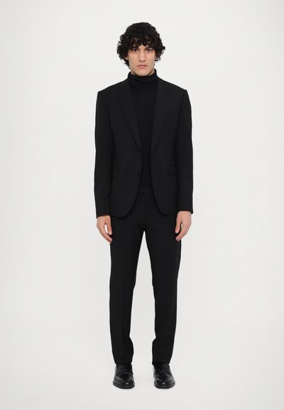 Schwarze Anzugjacke mit passendem Rollkragenpulli, taillierte Hose und glänzende schwarze Schuhe. Glatter Stoff mit einem eleganten, enganliegenden Design.