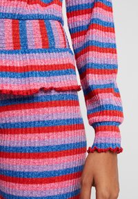 Dwu-częściowy zestaw z prążkowanego dzianiny z poziomymi paskami w kolorach czerwonym, różowym, niebieskim i fioletowym, z falbanami na mankietach i ozdobą w talii.