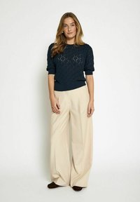 Cable-knit navy sweater with short sleeves, paired with high-waisted cream wide-leg trousers and dark brown slip-on shoes.
