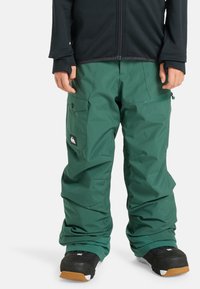 Groene waterdichte sneeuwbroek met een ontspannen pasvorm, met zijzakken, verstelbare boorden en een logopatch aan de voorkant.