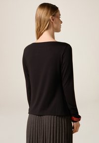 Czarna bluzka z długim rękawem, o szerokim, prostym dekolcie, wykonana z gładkiej tkaniny, zestawiona z teksturowaną, plisowaną szarą spódnicą.