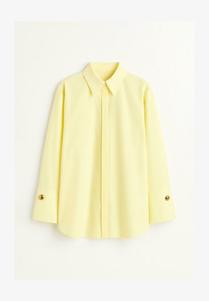 Sárga, hosszú ujjú ing könnyű anyagból. Klasszikus gallérral és arany gomb részletekkel a mandzsettákon. Sima textúra.