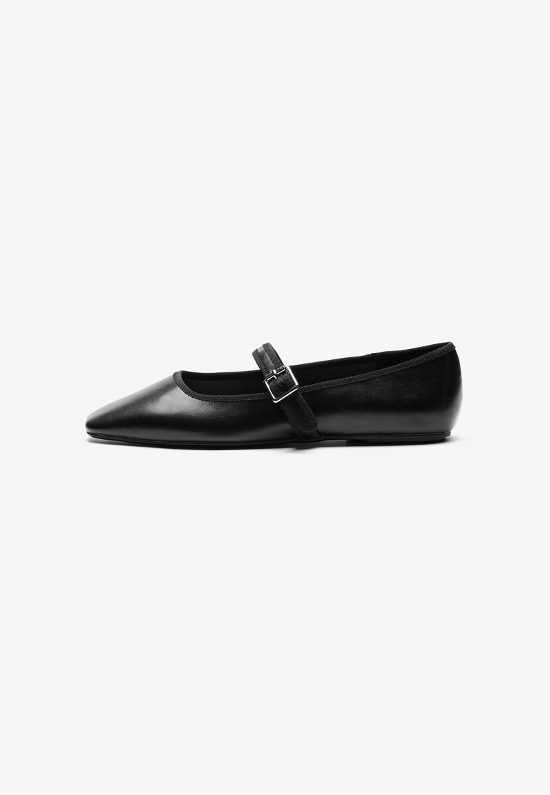 Chaussure plate en cuir noir avec bout pointu et bride réglable avec boucle argentée sur fond blanc uni.