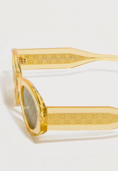 Κίτρινα διαφανή ορθογώνια γυαλιά ηλίου με διακοσμητικούς βραχίονες που φέρουν επαναλαμβανόμενα διπλά λογότυπα G.