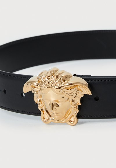 Must must nahkrihm, millel on suur kuldne metallsõlg klassikalise kuju kujutisega, millel on detailne juuksed ja tiivad.