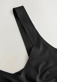 Fekete szövet bralette széles pántokkal és V-alakú nyakkivágással. Simaság jellemzi, minimális varrási részletekkel.