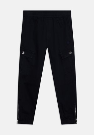 Schwarze Cargo-Hosen mit elastischem Bund, seitlichen Taschen, Reißverschluss-Akzenten an den Knöcheln und einem dezenten Logo-Patch auf der Vorderseite.
