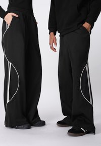 Fekete, széles szárú nadrág fehér díszítő vonalakkal. Rugalmas derékpánttal és oldalzsebekkel rendelkezik. Az anyaga sima és kényelmes, laza szabású.