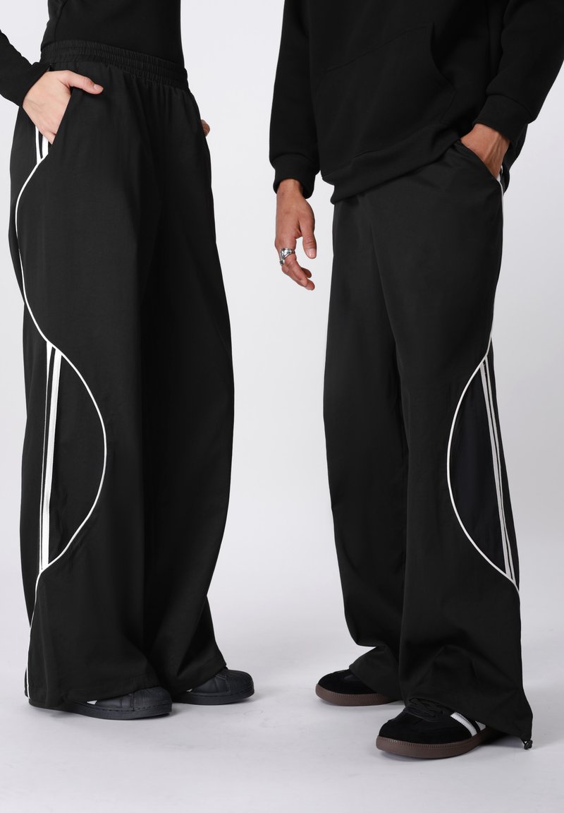 Fekete, széles szárú nadrág fehér díszítő vonalakkal. Rugalmas derékpánttal és oldalzsebekkel rendelkezik. Az anyaga sima és kényelmes, laza szabású.