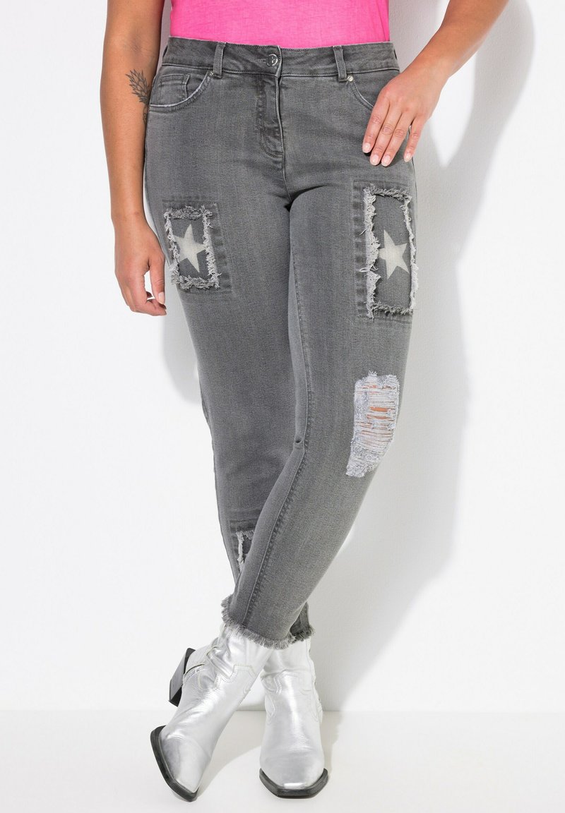 Jeans gris desgastados con parches de estrellas, bordes deshilachados y un corte ajustado, combinados con botas de tobillo plateadas brillantes.