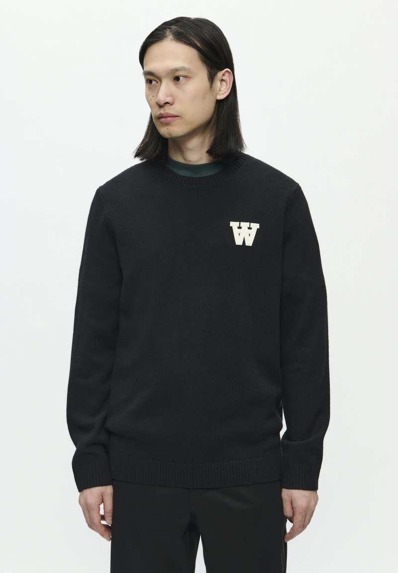 Schwarzer Strickpullover mit gerippten Bündchen und Saum, mit einem cremefarbenen "W"-Logo auf der Brust. Glatte Textur mit Rundhalsausschnitt.