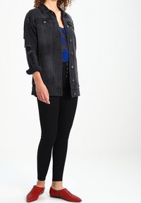 Czarna kurtka dżinsowa z postrzępionymi detalami, na niebieskiej, wzorzystej bluzce, w połączeniu z czarnymi legginsami i czerwonymi balerinami, podkreślająca różnorodne tekstury.