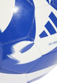 Niebieska i biała piłka nożna z błyszczącą syntetyczną powierzchnią, zdobiona ostrymi, zygzakowymi wzorami oraz napisem brandingowym "TIRO CLUB."