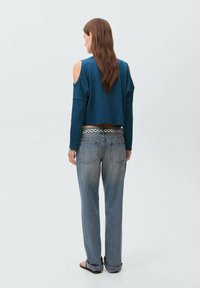 Zelenkasto modra pulover s skrajšanimi rokavi in izrezanimi rameni, v kombinaciji s svetloblujimi kavbojkami, ki imajo okrasni pas. Model ima dolge rjave lase.