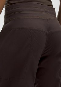 Pantaloni atletici de culoare maron închis, cu un tiv înalt texturat, având cusături orizontale și o țesătură netedă. Croi ajustat pe corp.