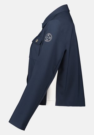 Veste marine à la coupe structurée, avec une poche poitrine, une texture lisse et un accent décoratif sur la manche gauche.