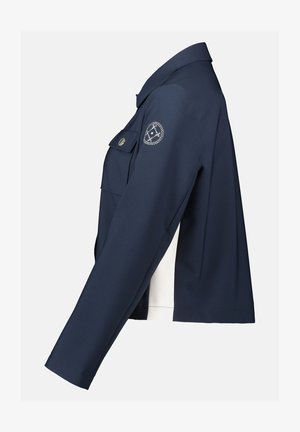 Granatowa kurtka o wyraźnie zarysowanym kroju, z kieszenią na piersi, gładką teksturą oraz ozdobnym akcentem na lewym rękawie.