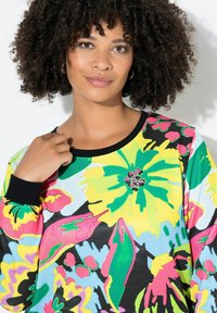 Sweatshirt coloré avec des motifs floraux vibrants en jaune, rose, vert et noir. Encolure et poignets côtelés, texture de tissu douce.
