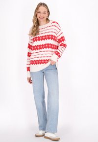 Rot und weiß gemusterter Pullover mit geometrischen Designs, kombiniert mit hellblauen Jeans und weißen Sneakers. Glatte Stricktextur und lockere Passform.